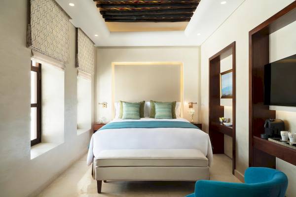 Innenansicht eines Zimmers im Souq Al Wakra Hotel Qatar By Tivoli mit einem großen Bett, Fenstern und modernen Möbeln.