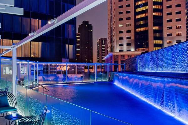 Nachtansicht des Swimmingpools im W Doha Hotel & Residences mit blauer Beleuchtung und umliegenden Gebäuden.