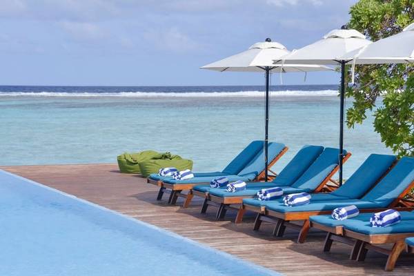 Am Pool der Summer Island Maldives stehen blaue Lounge-Stühle mit weißen Sonnenschirmen.
