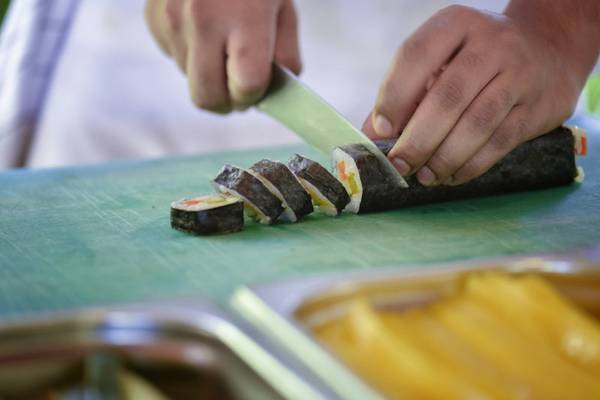Person schneidet Sushi auf einem grünen Schneidebrett im Hotel Summer Island Maldives.