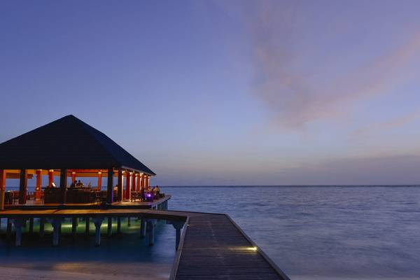 Hotelterrasse des Summer Island Maldives bei Sonnenuntergang, mit leuchtenden Lichtern und Blick aufs Meer.
