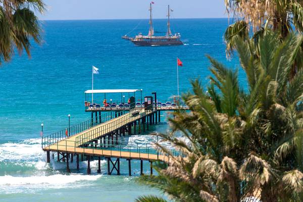 Turquoise Hotel Pier mit einem Boot im Hintergrund, umgeben von Palmen und Wasser.