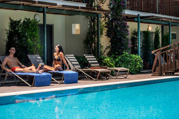 Ein Mann und eine Frau sitzen auf Liegestühlen neben dem Pool des Turquoise Hotels.