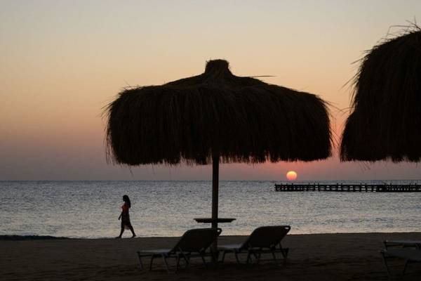 Sonnenuntergang am Strand mit Sonnenschirmen und einer Person, die in der Ferne geht