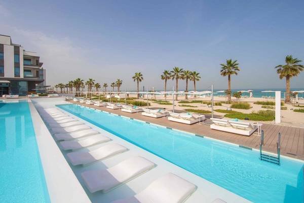 Außenpool des Nikki Beach Resort & Spa Dubai mit weißen Liegestühlen und Blick auf den Strand