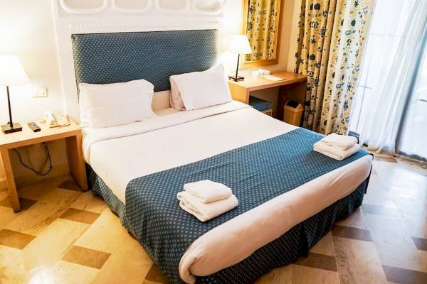 Schlafzimmer im Grand Hotel Sharm El Sheikh mit einem Doppelbett, Nachttischen, Lampen und einer Kommode.