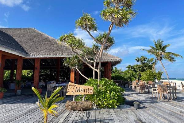 Foto der Außenterrasse des Brennia Kottefaru Maldives Hotels mit Holzboden, Tischen, Stühlen und Palmen.