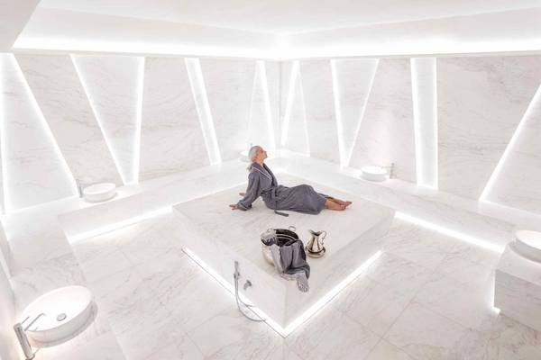 Eine ältere Frau sitzt entspannt in einem weißen Marmor-Spa-Raum des Nikki Beach Resort & Spa Dubai.