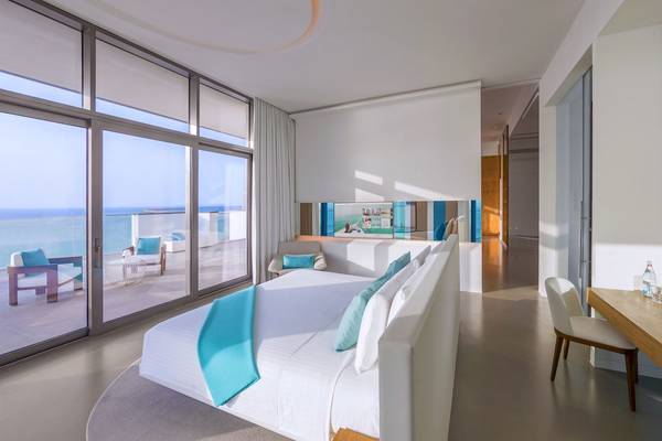 Ein modernes Hotelzimmer mit einem Bett, Blick auf das Meer und einer großen Glaswand.