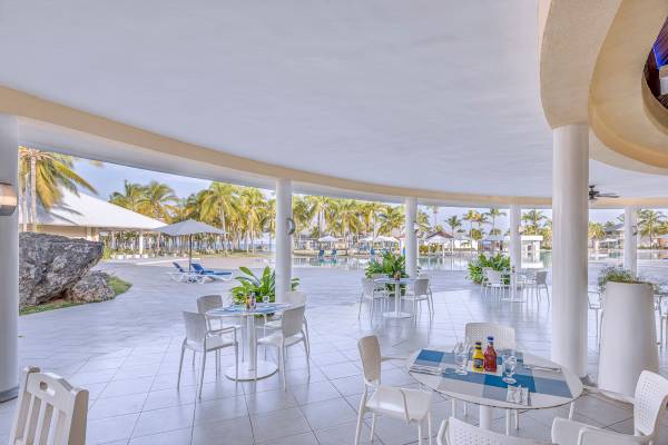 Terrasse des Paradisus Varadero Resorts mit weißen Tischen und Stühlen, Blick auf den Pool und Palmen