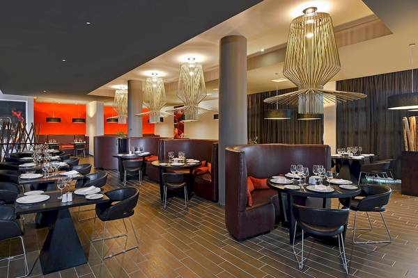 Innenansicht eines modernen Hotelrestaurants mit dunklen Möbeln und großen Leuchten.