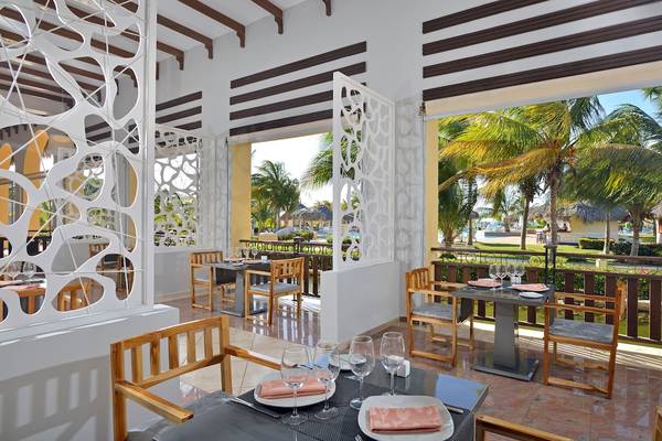 Innenansicht des Restaurants im Paradisus Varadero Resort & Spa mit Tischen, Stühlen und Blick auf Palmen und den Pool