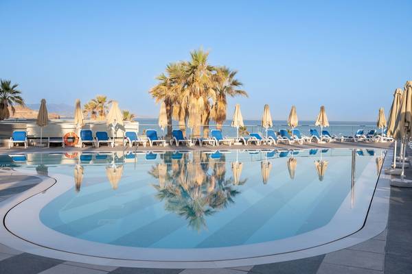 Ein Swimmingpool im Arina Beach Resort mit blauen Sonnenliegen und Palmen.