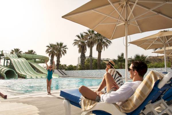 Familie am Pool des Arina Beach Resorts, mit Wasserrutschen und Palmen im Hintergrund.