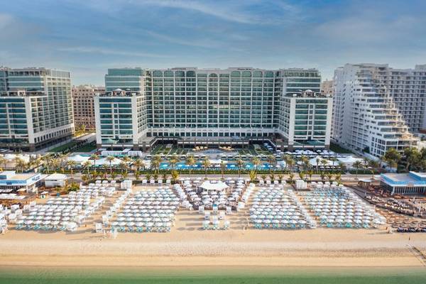 Außenansicht des Hilton Dubai Palm Jumeirah Hotels mit Swimmingpool und vielen Sonnenschirmen am Strand