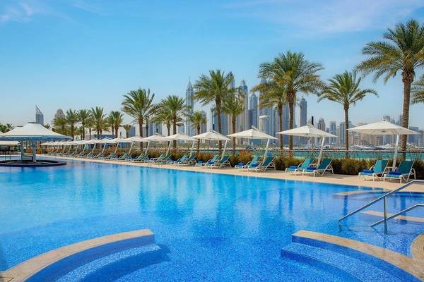 Außenpoolbereich des Hilton Dubai Palm Jumeirah Hotels mit blauen Sonnenliegen und Palmen