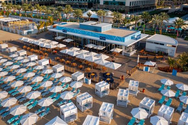 Luftaufnahme des Hilton Dubai Palm Jumeirah Hotels mit Strandlounge, Sonnenschirmen und Liegestühlen.