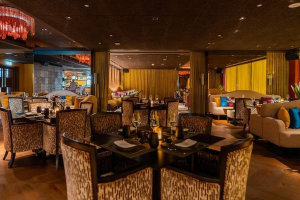 Innenbereich des Hilton Dubai Palm Jumeirah Restaurants mit gemusterten Stühlen und Tischen, gelben Vorhängen und rotem Kronleuchter.