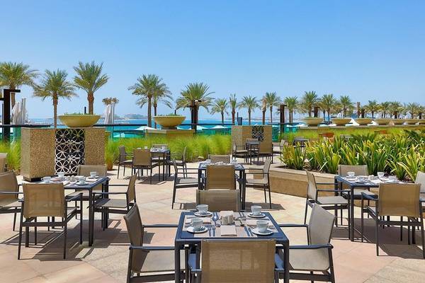 Außenbereich des Restaurants im Hilton Dubai Palm Jumeirah mit Tischen, Stühlen und Blick auf das Meer.