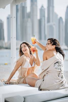 Zwei Frauen am Strand im Hilton Dubai Palm Jumeirah, die Cocktails genießen.
