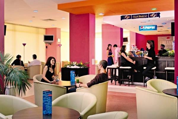 Ein Hotel-Loungebereich mit Tischen und Stühlen, in dem Gäste sitzen und Getränke genießen.