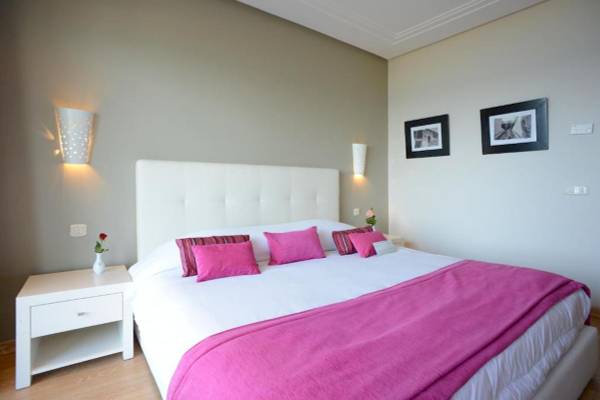 Schlafzimmer im Nozha Beach & Spa Hotel mit einem großen Bett, rosa Decken, weißen Kissen und Wanddekorationen.