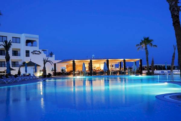 Abendansicht des Swimmingpools des Nozha Beach & Spa Hotels mit Beleuchtung und Liegestühlen.