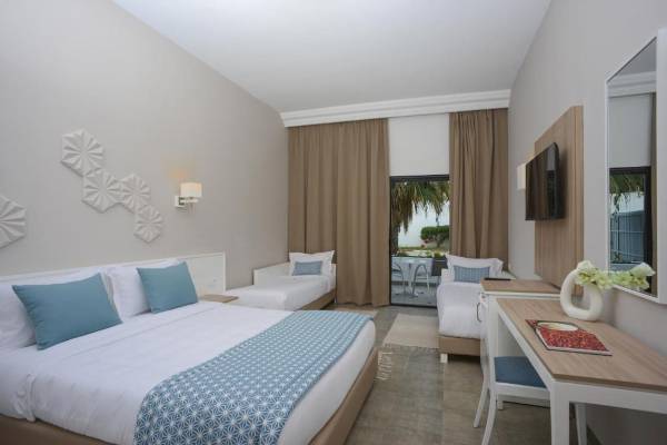 Innenansicht eines Zimmers im Nozha Beach & Spa Hotel mit drei Betten, Schreibtisch und Fernseher.