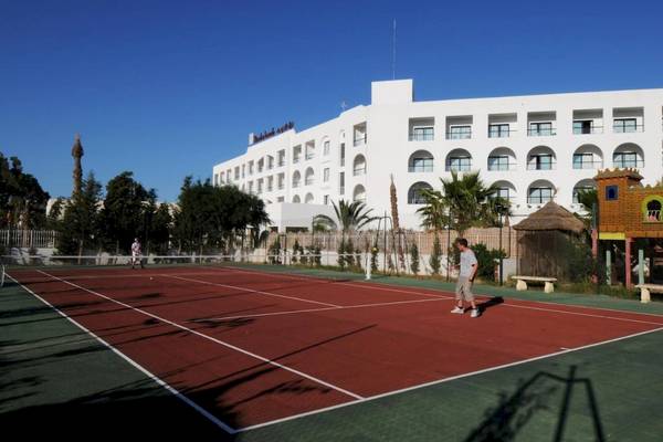 Tennisplatz vor dem Nozha Beach & Spa Hotel mit zwei Spielern und einer Person, die zuschaut.