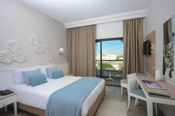 Innenansicht eines Hotelzimmers im Nozha Beach & Spa mit Bett, Schreibtisch und Balkon.