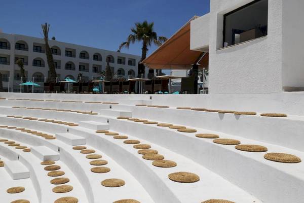 Weiße Sitzplätze vor dem Nozha Beach & Spa Hotel mit Blick auf eine Terrasse und Palmen.