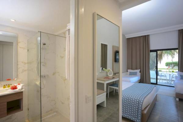 Innenansicht eines Hotelzimmers im Nozha Beach & Spa Hotel mit Dusche, Bett und Schreibtisch.