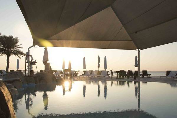 Sonnenuntergang am Poolbereich des Sealine Beach, A Murwab Resort mit Liegestühlen und Sonnenschirmen.