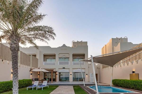 Außenbereich des Sealine Beach, A Murwab Resort mit Swimmingpool, Sonnenliegen und Palme.