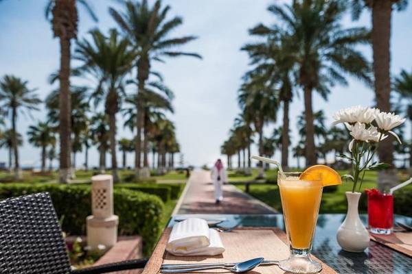 Frühstückstisch im Sealine Beach, A Murwab Resort mit Blick auf eine Allee von Palmen und einem Glas Orangensaft