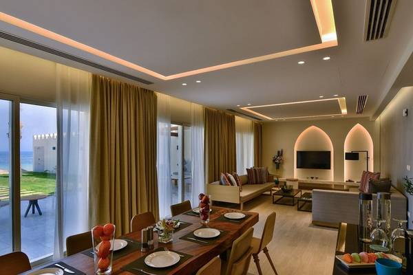 Wohnbereich des Sealine Beach, A Murwab Resort mit Esstisch, Couch, Fernseher und Meerblick.
