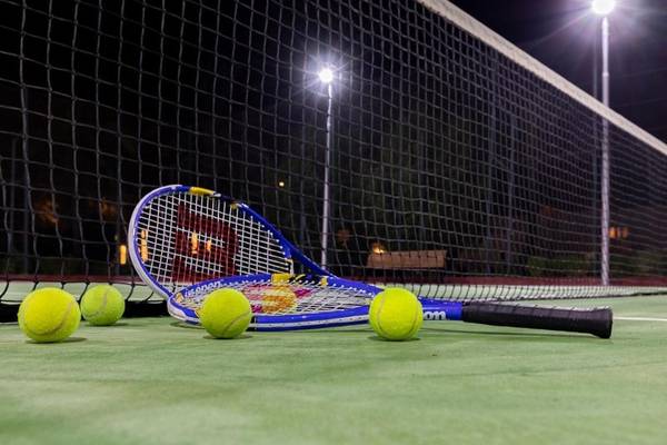 Tennisplatz mit Schläger und Bällen bei Nachtbeleuchtung
