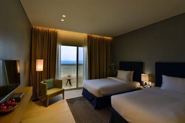 Hotelzimmer im Sealine Beach, A Murwab Resort mit zwei Betten, Fernseher, Fenster und Balkon.