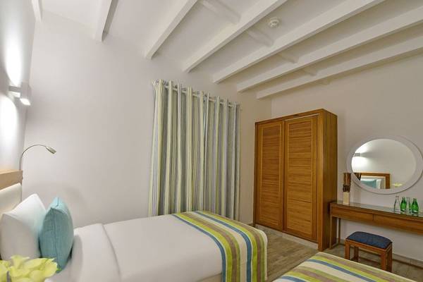 Zwei Betten Zimmer im Sealine Beach, A Murwab Resort mit weißem Interieur, blauen Kissen und einem runden Spiegel.