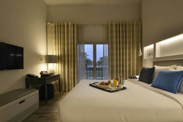 Innenansicht eines Hotelzimmers von Sealine Beach, A Murwab Resort mit Bett, Frühstückstablett, Fernseher und Balkon.