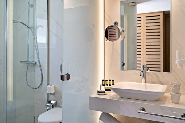 Innenansicht eines Badezimmers im Pilot Beach Resort mit einer Glasdusche, einem Waschbecken, einem Spiegel und einer Toilette.