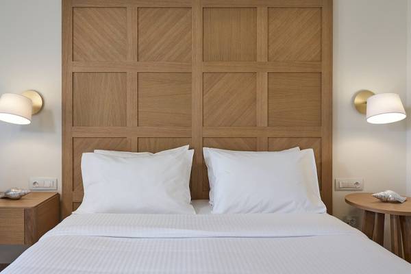 Schlafzimmer im Pilot Beach Resort mit einem großen Bett, weißen Laken, Kissen und einem großen Holzkopfteil.
