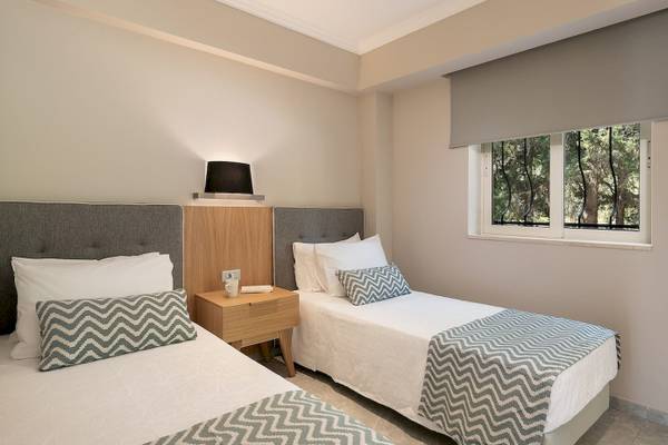 Innenansicht eines Doppelzimmers im Pilot Beach Resort mit zwei Betten, Nachttischen und Fenstern, die auf einen Garten blicken.