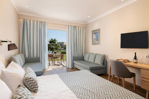 Innenansicht eines Hotelzimmers im Pilot Beach Resort mit Doppelbett, Sofa, Schreibtisch und Terrassenzugang.