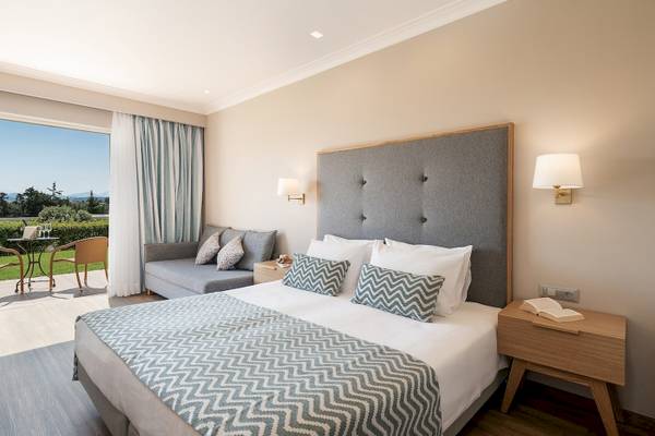 Hotelzimmer im Pilot Beach Resort mit großem Bett, grauem Kopfteil, Couch und Fenster mit Blick auf Garten