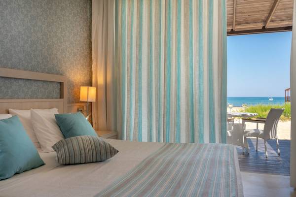 Zimmer im Pilot Beach Resort mit Blick auf das Meer, Bett mit blauen Kissen und Tisch mit Stühlen auf der Terrasse.