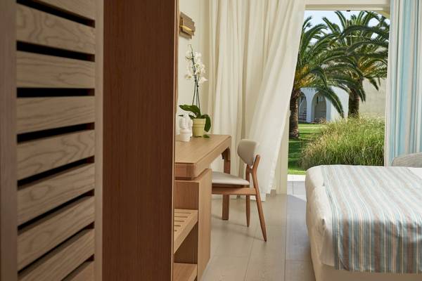Innenansicht eines Zimmers im Pilot Beach Resort mit Schreibtisch, Stuhl, Blumen und Blick auf Palmen und Rasen.