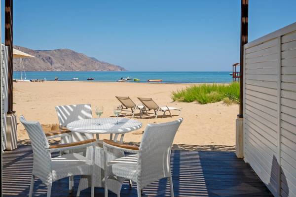 Terrasse des Pilot Beach Resorts mit Tisch und Sesseln am Strand, Blick aufs Meer.