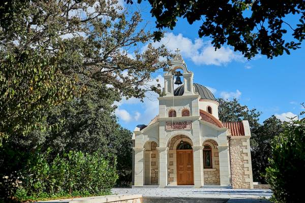 Kleine Kirche mit Glocke und Kuppel umgeben von Bäumen und Sträuchern
