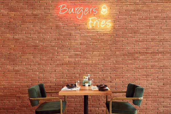 Ein Tisch im Restaurant vor einer Ziegelwand mit der Neonschrift 'Burgers & Fries'.